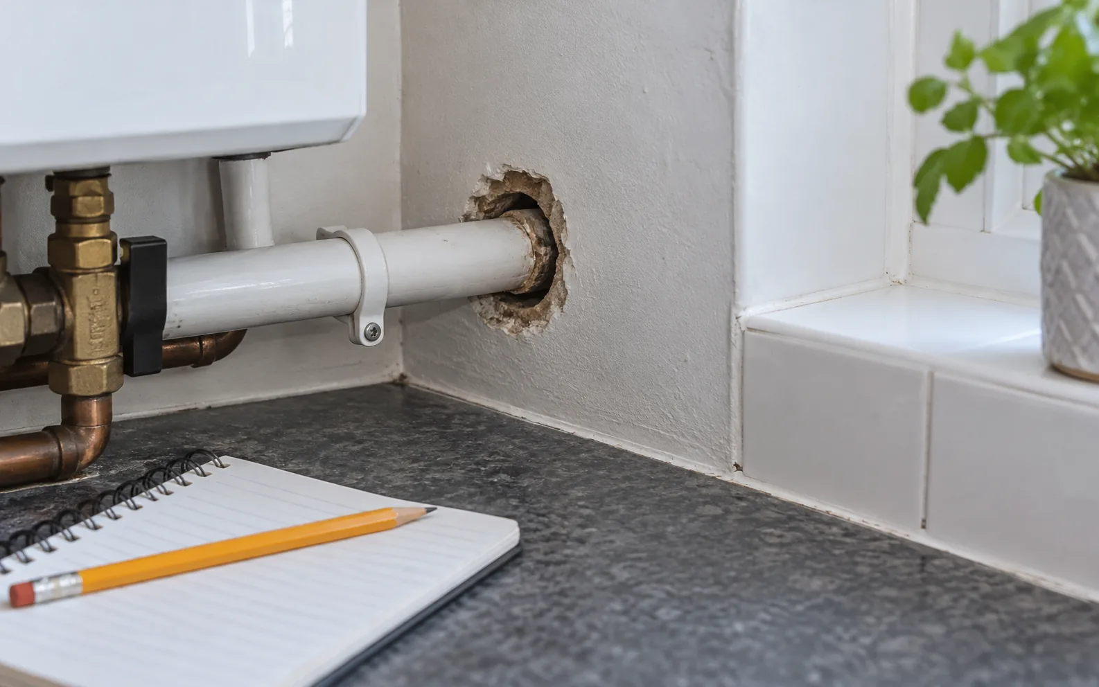 Unsealed gap around a kitchen utility pipe beside an inspection notebook